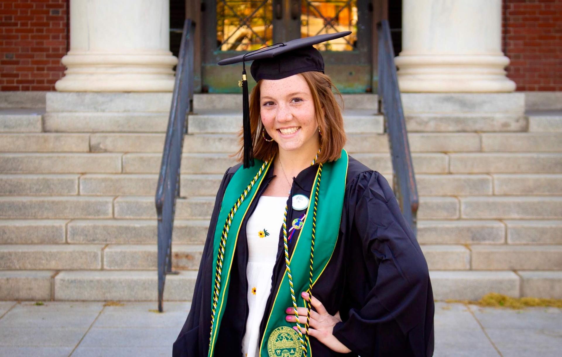 Claire Lennon dressed in regalia on campus in front of Waterman Building.