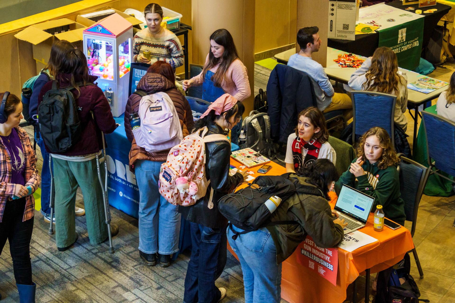 An overhead shot of multiple students interacting with various tables on the ground level, many people talking and interacting while a few show off things that their table is showcasing