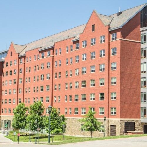 A seven-story, brick residence hall with trees and grass in the foreground.