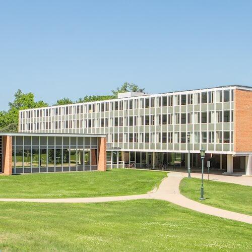 A four-story residence hall with a wall of windows next to a green lawn space. 