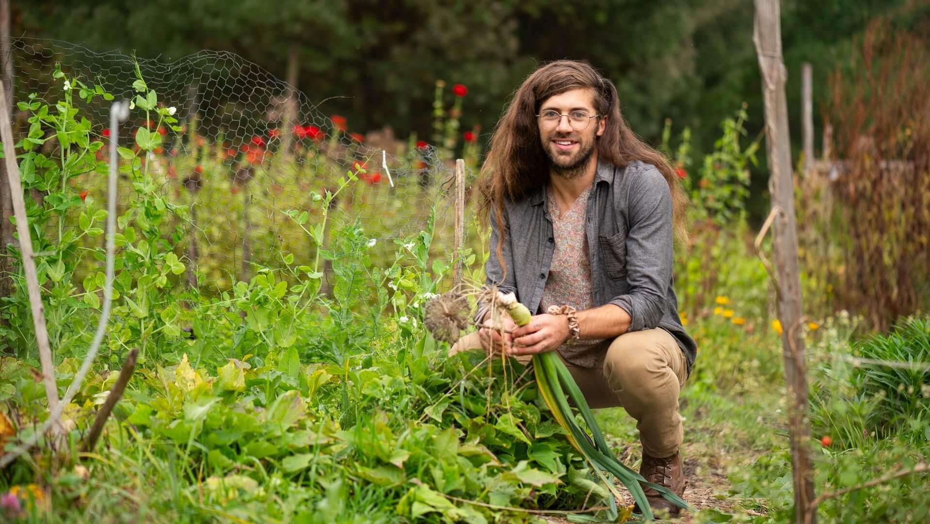 Former PhD student Sam Bliss crouching in a garden holding an onion