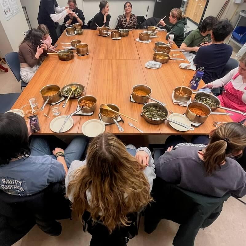 A birds-eye shot of students sharing a meal with pots and bowls of various food. 