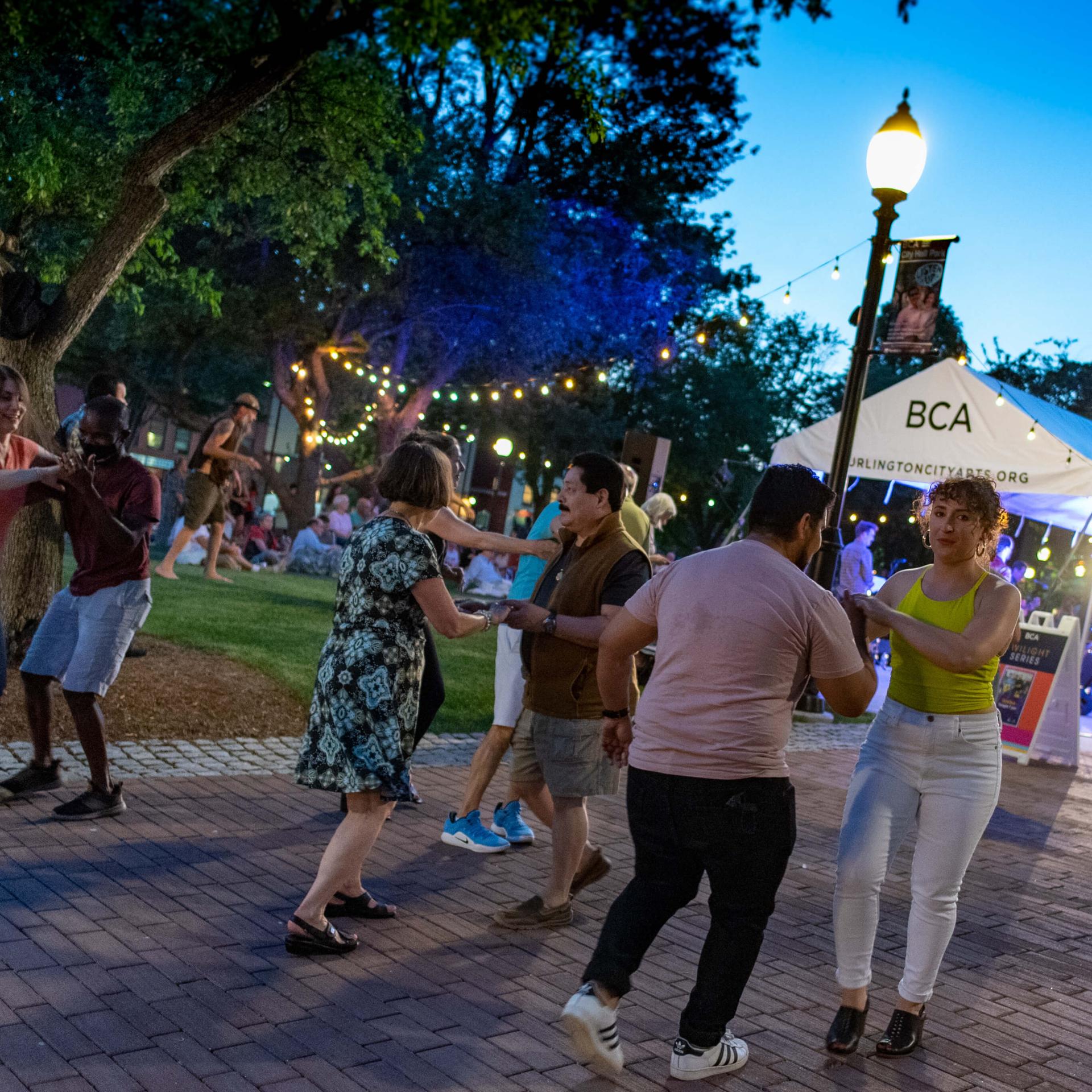 People of different races wearing summery clothing salsa dancing in downtown Burlington in the early evening