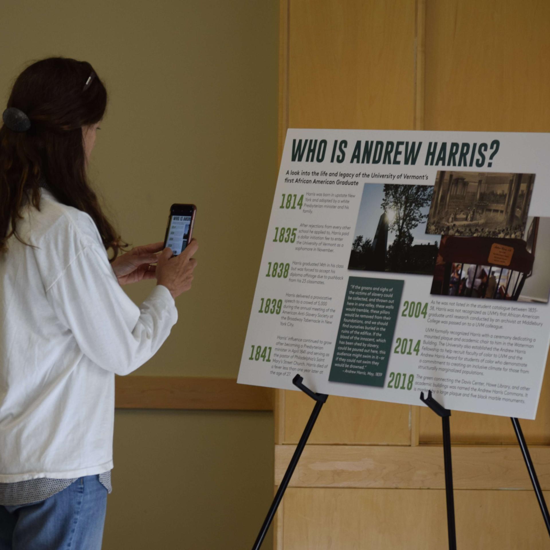 A person taking a picture of a poster that's titled "Who is Andrew Harris?" A timeline can be seen along with photos on the poster.