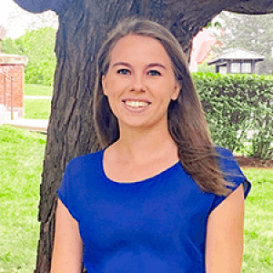 Bethany, dressed in vibrant blue, standing under a tree