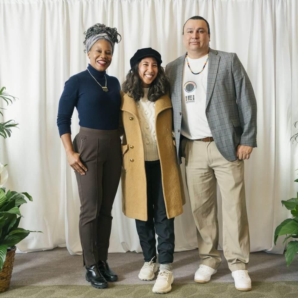 Majora Carter, Kristy Drutman, and Cody Two Bears pose for a photo in front of a white back drop.