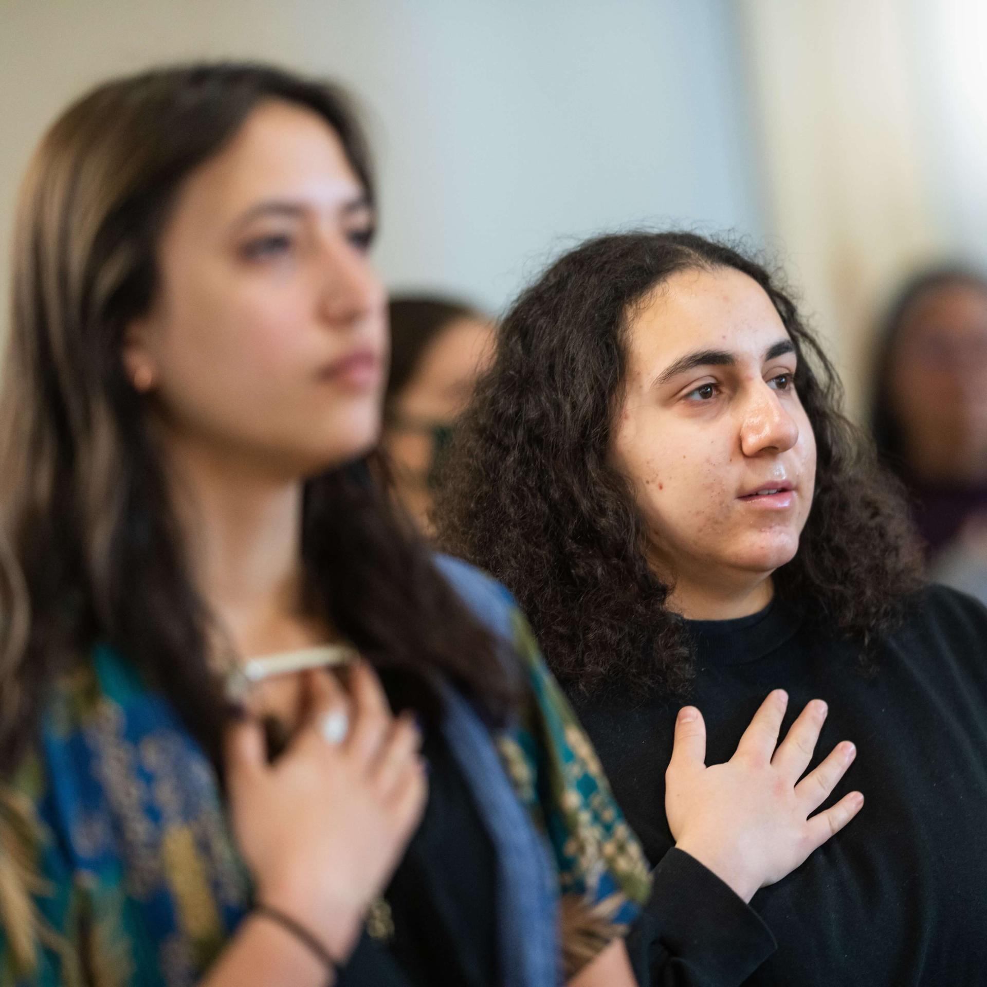 Two women hold their hands to their hearts.