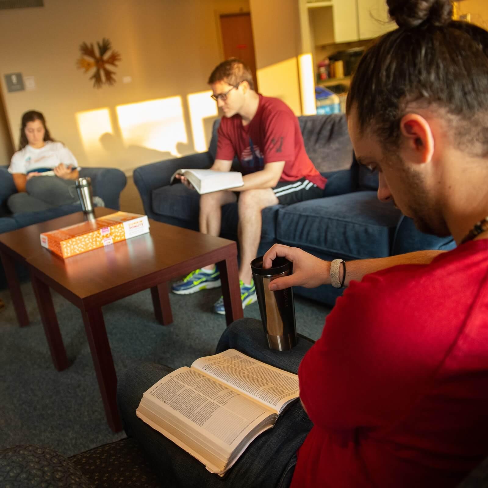 Three people sit in a sunny lounge reading.