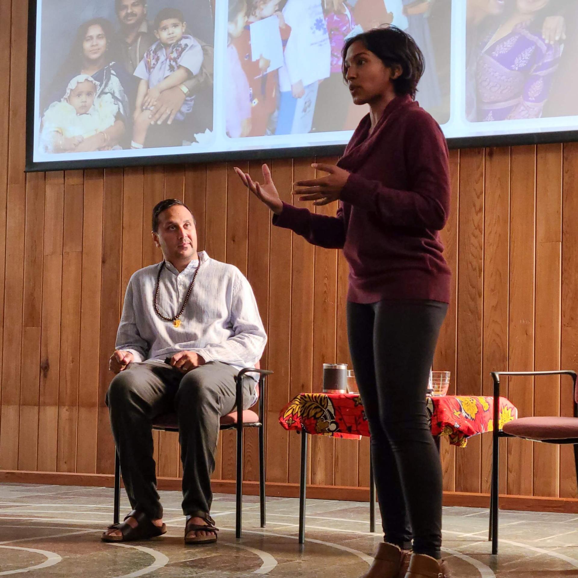 Vice Provost Ahmed sits and listens to his co-presenter on as she stands and speaks in the Interfaith Gathering Hall