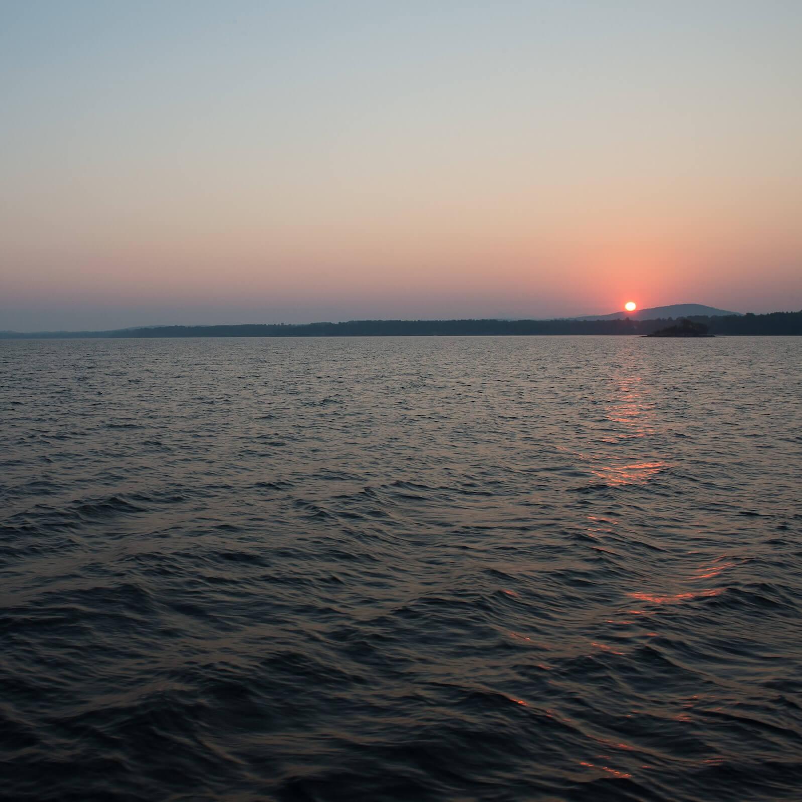 Lake Champlain with the sun setting behind a mountain in the distance.