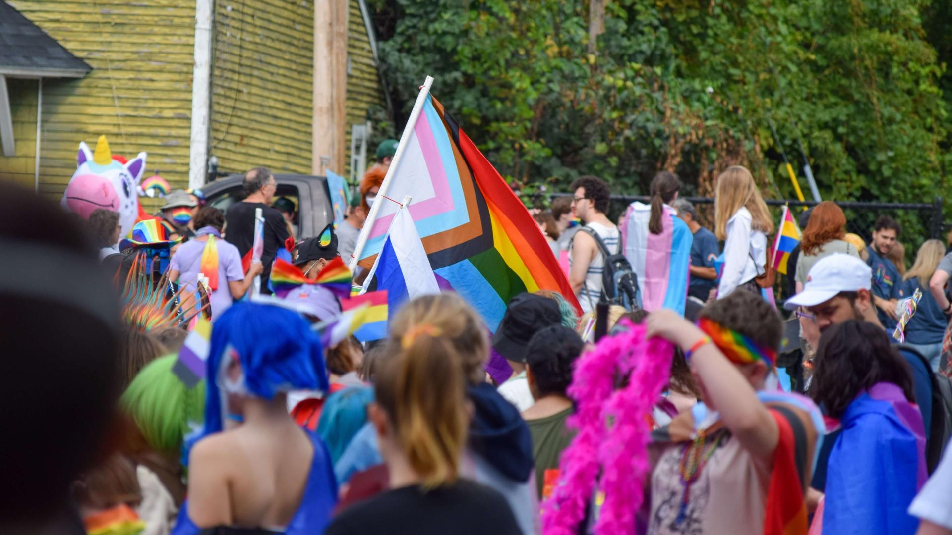 A vibrant UVM constituency marches in Burlington's Pride parade. An inclusive LGBTQ+ Pride flag is in focus among the sea of people.