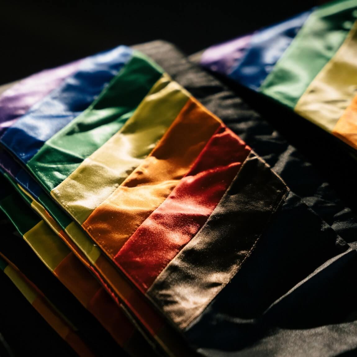 Two stacks of rainbow graduation stoles reflecting light in a dark room.