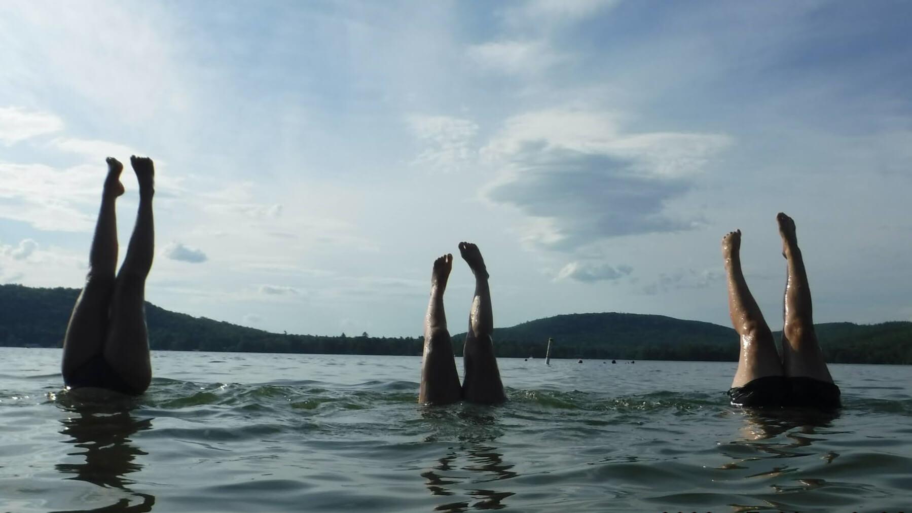 Three pairs of legs emerge from Lake Champlain as students do handstands below water