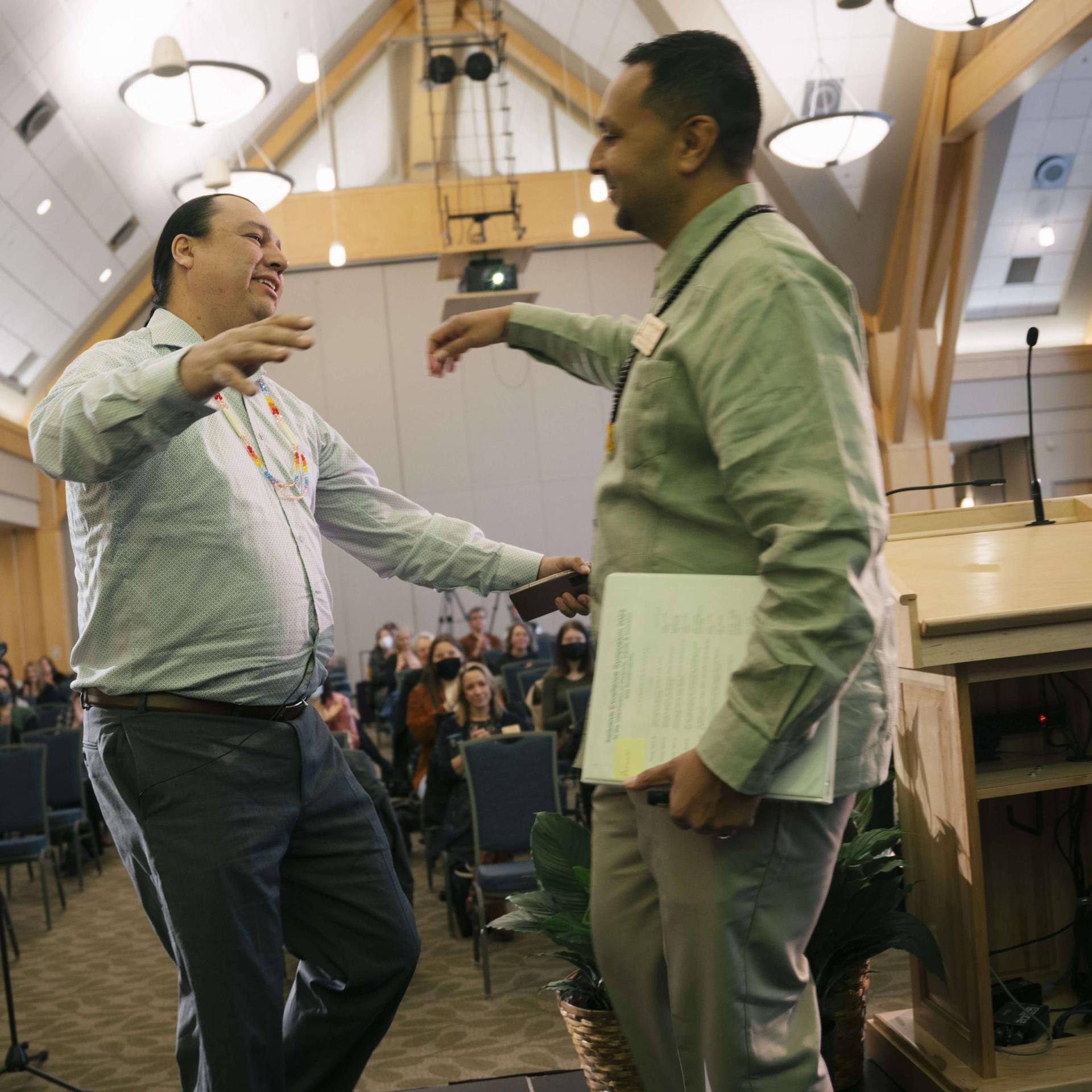 Vice Provost Amer walking into hug speaker Cody Two Bears in front of a crowd.