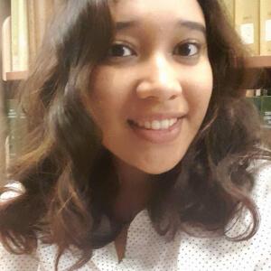 A smiling Vanessa in an indoor setting with book lined shelves behind her.