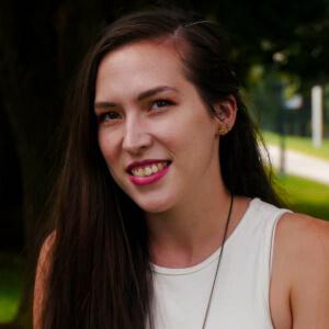 Emily, smiling with a bright red lip and green grass in the background