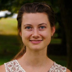 Rachel, hair pulled back, smiling with green grass and trees in the background