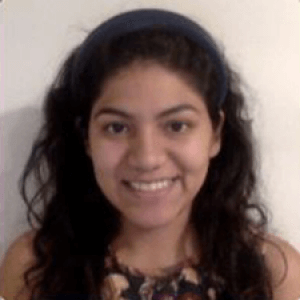 Raquel, smiling for the camera, against a neutral, indoor background