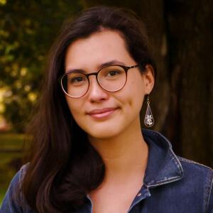 Rhiannon, wearing a small smile, outdoors, under a tree