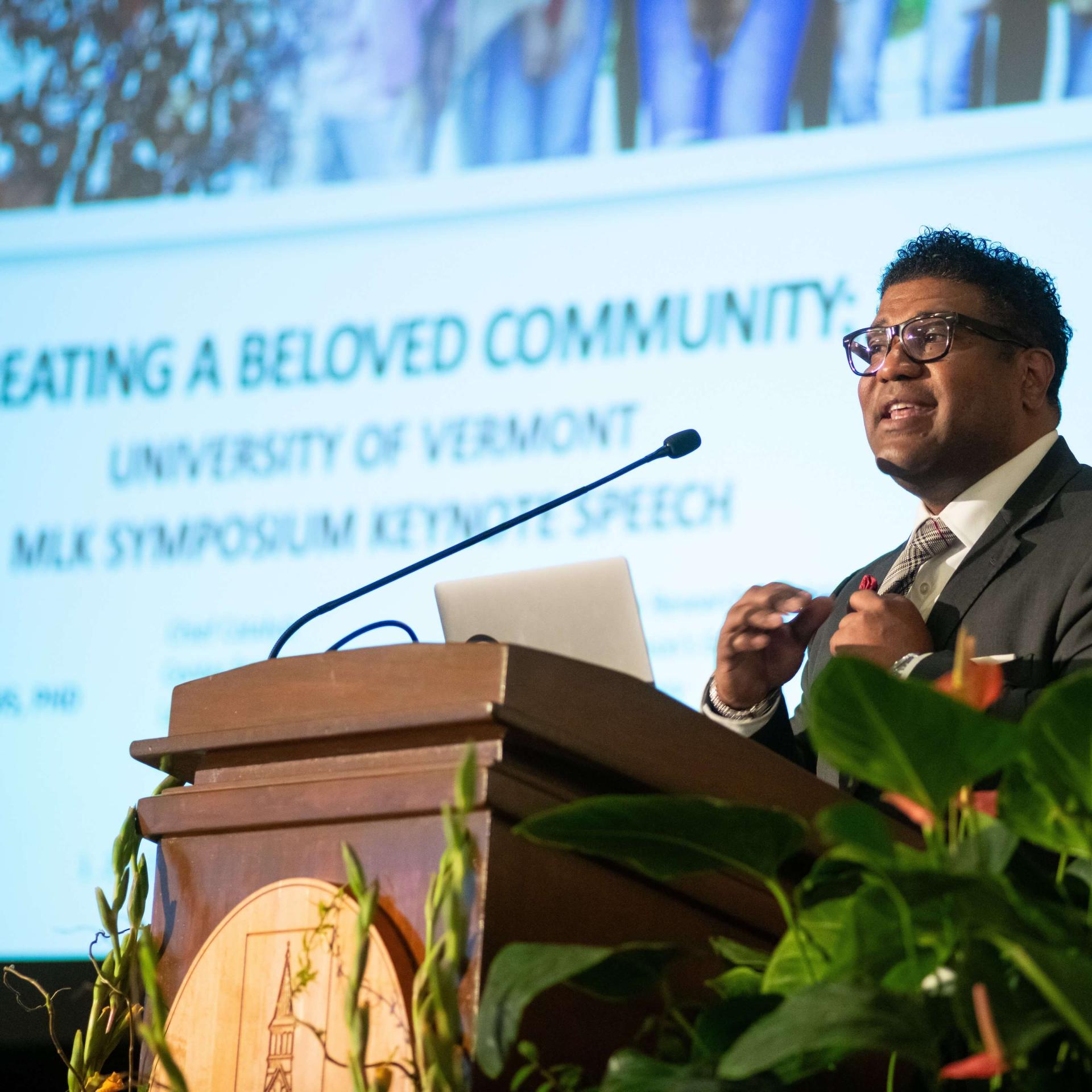 Damon Williams at a podium with a slide projected behind him that reads, Creating a Beloved Community UVM MLK Symposium Keynote Speech