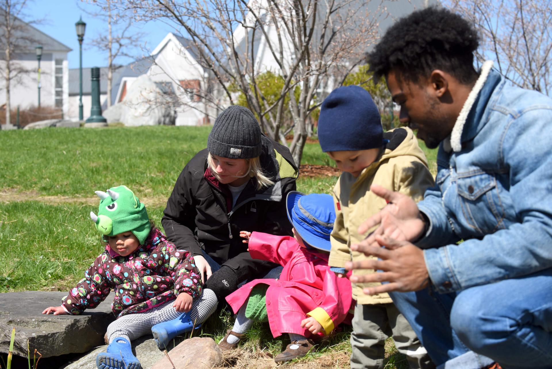 Young children and their caregivers playing outdoors together.