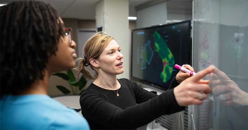 A professor and student discuss data science at a white board