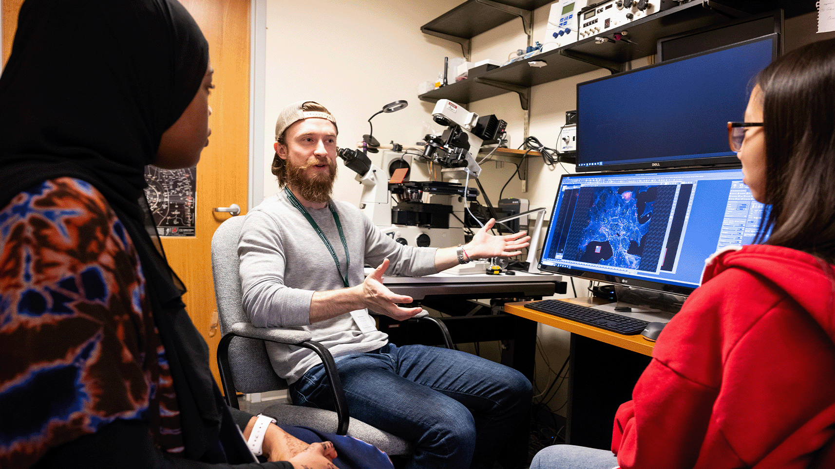 Researcher shows two students microscope images in the Cunniff Lab at the UVM Cancer Center. 