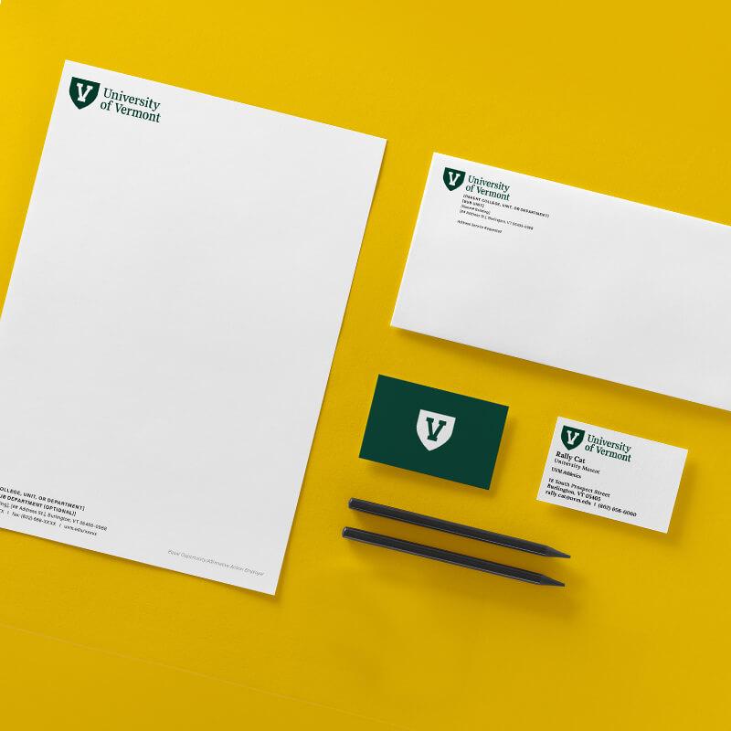 examples of letterheads, envelopes, and business cards branded with the uvm logo against a yellow background