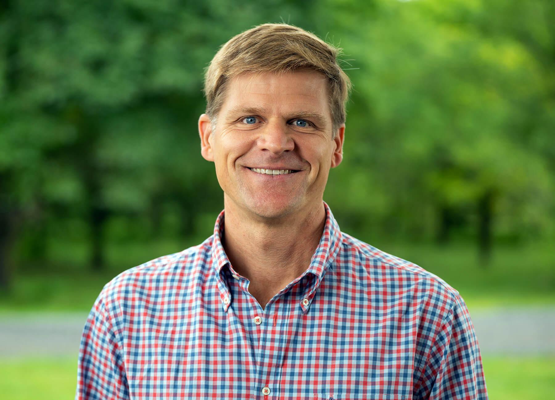 Mark Isselhardt outdoors, smiling, wearing a checked oxford shirt