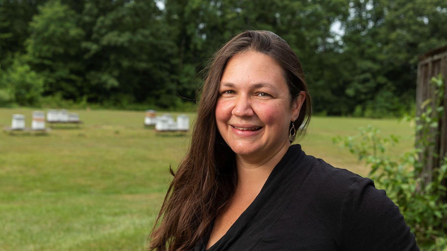 Kaira Wagoner smiles. In the background are several honeybee colonies.