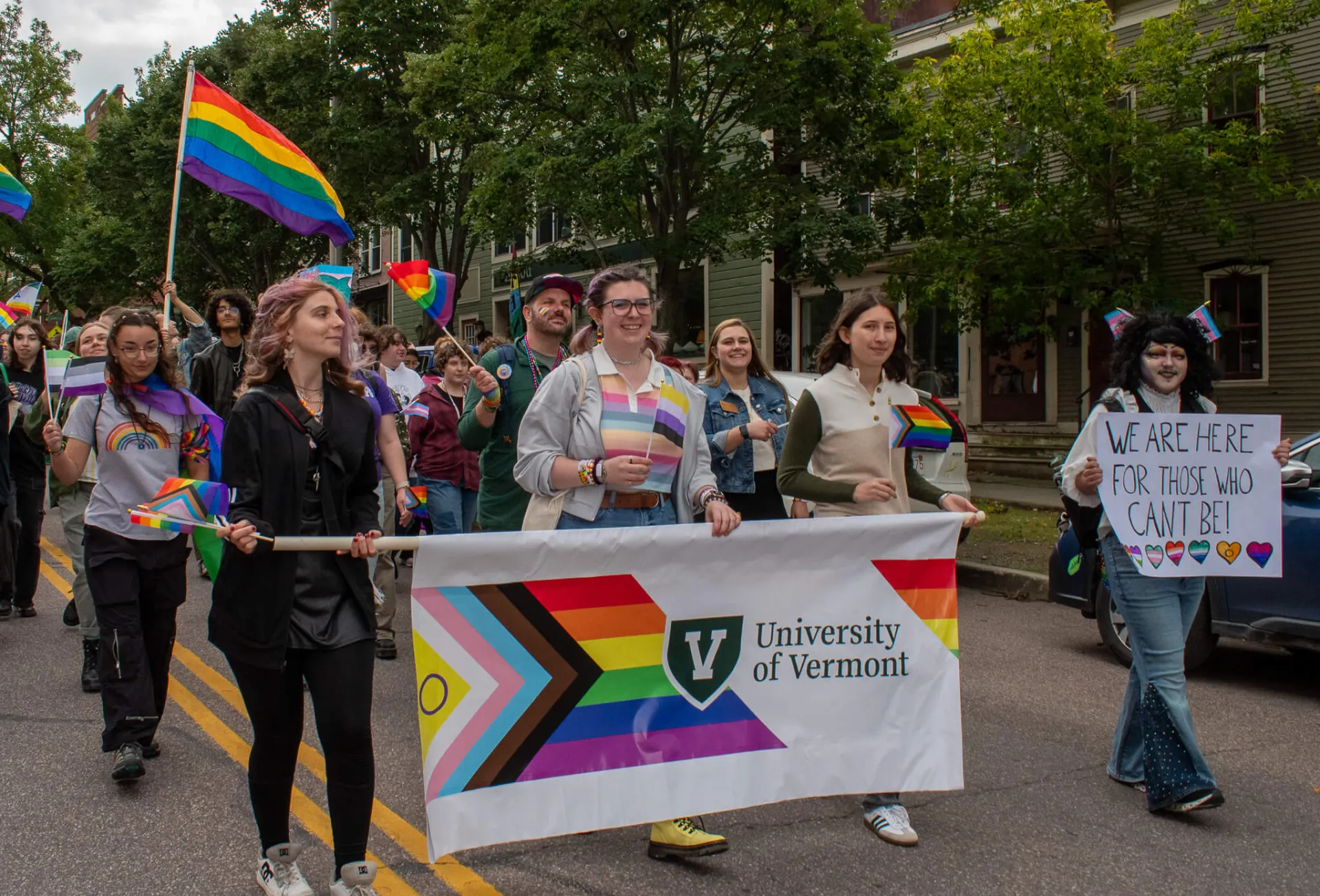 People walk at the parade holding rainbow flag and UVM rainbow banner