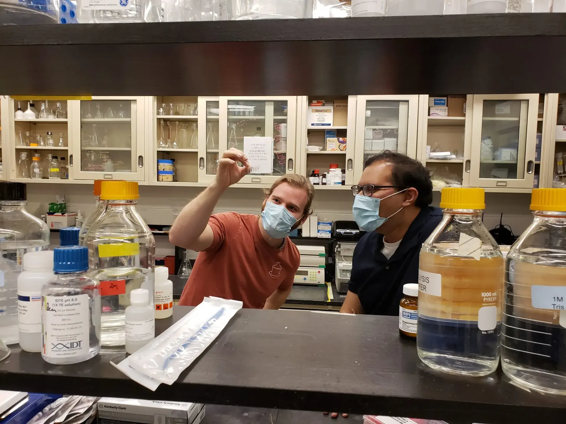 Dev Majumdar and Zach Miller inspect a small vial in their lab