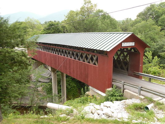A red covered bridge spanning a gorge surrounded by lush greenery