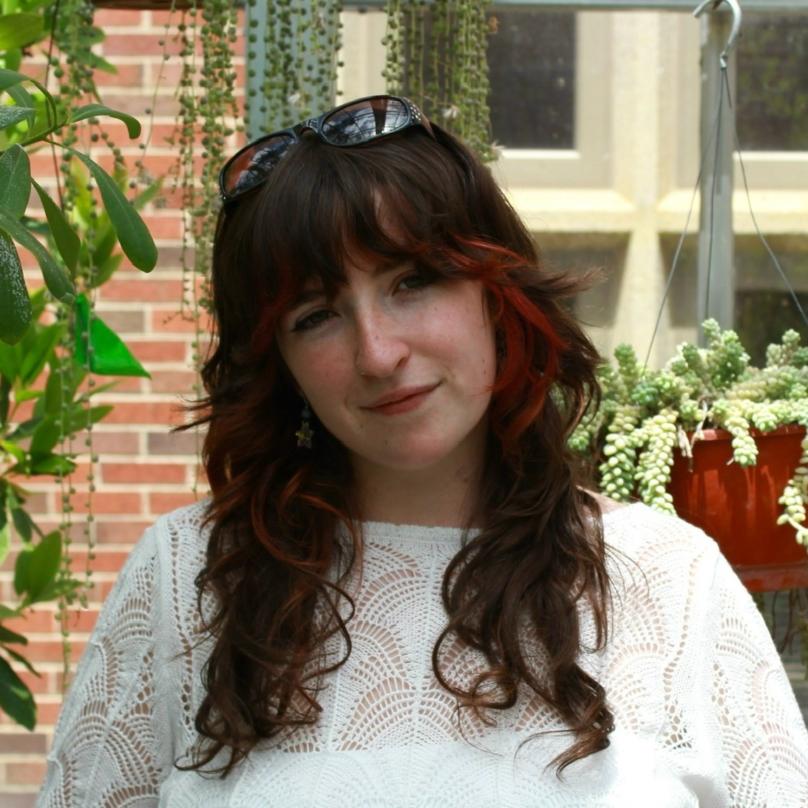 Allie standing in front of a brick wall with plants surrounding her.